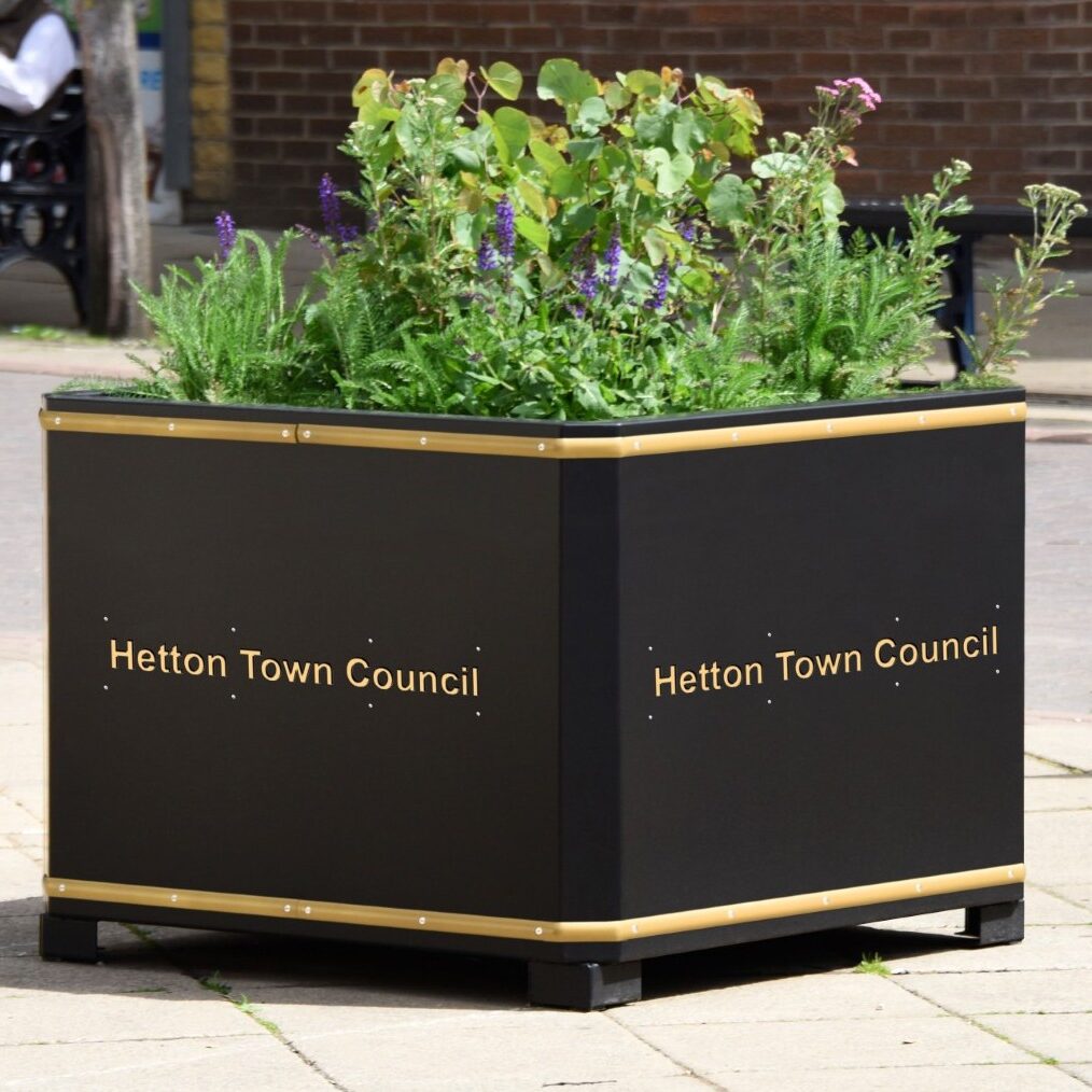 Large black planter labeled Hetton Town Council, filled with green plants and flowers.